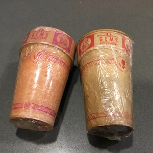 May include: Two brown paper cups with red and white labels that say "Flavor-Sealed Gems A Little Treat For You" and "Gems" with a picture of a woman on the label. The cups are wrapped in clear plastic.