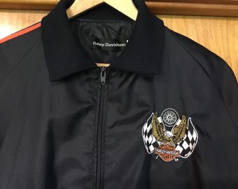 May include: Black Harley-Davidson jacket with a zipper closure and an embroidered logo featuring a winged eagle, checkered flags, and the text "Motor? Harley-Davidson? Cycles".