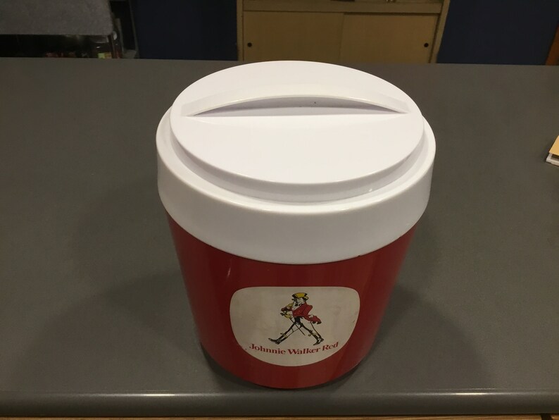 May include: Red and white cooler with a white lid and a Johnnie Walker Red label featuring a man in a walking pose.