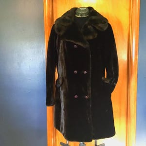 May include: A black faux fur coat with a large collar and double breasted closure. The coat has three buttons and is lined with a smooth fabric.