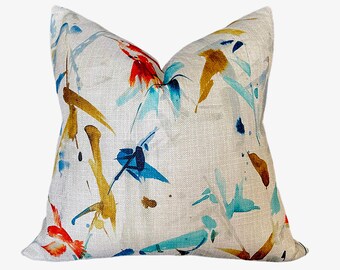 May include: A white throw pillow with a colorful abstract design featuring blue, turquoise, yellow, and red paint splatters and brushstrokes.