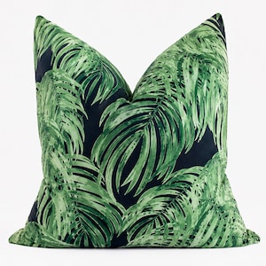 May include: A square throw pillow featuring a vibrant botanical print of large, overlapping palm leaves in various shades of green set against a deep, solid black background. The fabric displays a smooth texture with a distinct leaf pattern.