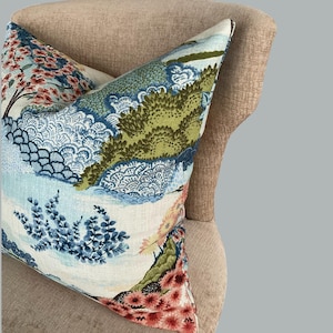May include: A decorative pillow with a blue, green, and pink floral pattern. The pillow is on a light brown chair.