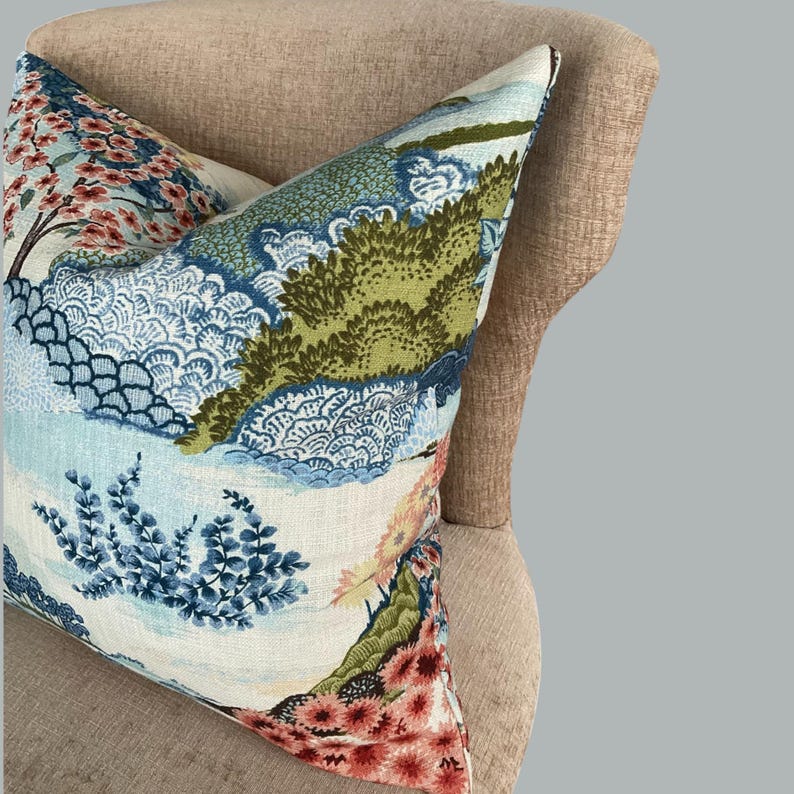 May include: A decorative pillow with a blue, green, and pink floral pattern. The pillow is on a light brown chair.