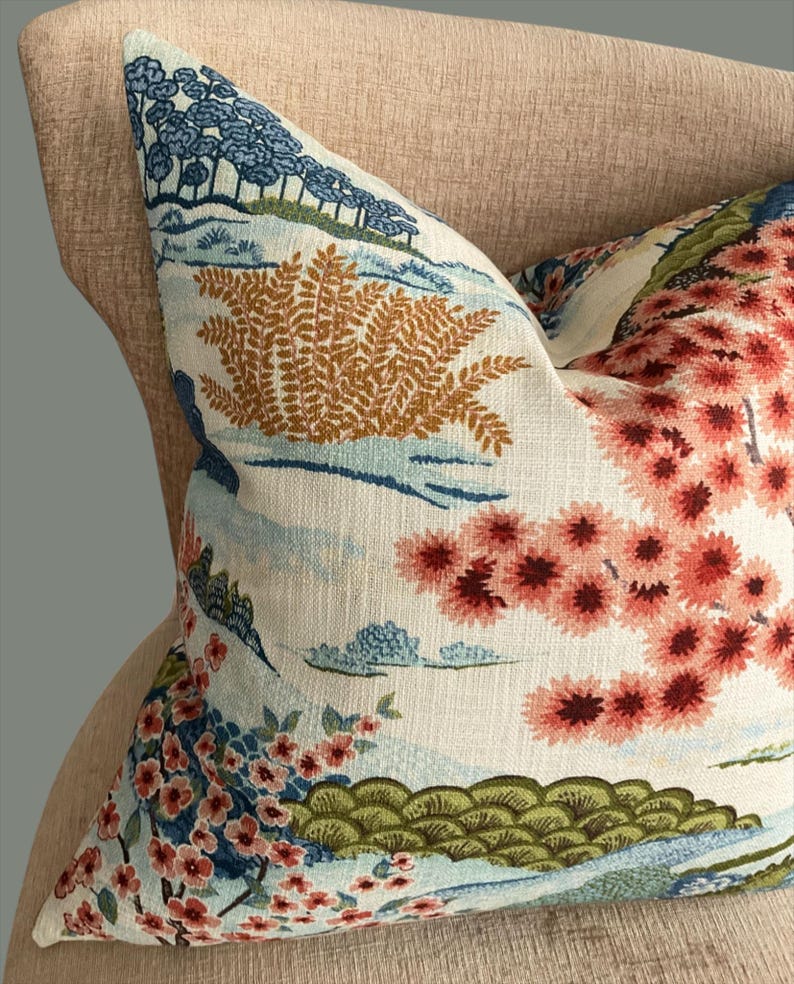 May include: A decorative throw pillow with a floral pattern featuring pink, blue, and green flowers on a white background. The pillow has a light blue and brown fern pattern in the upper left corner.