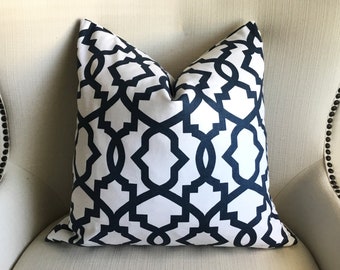 May include: A white throw pillow with a navy blue geometric pattern. The pillow is sitting on a white armchair.
