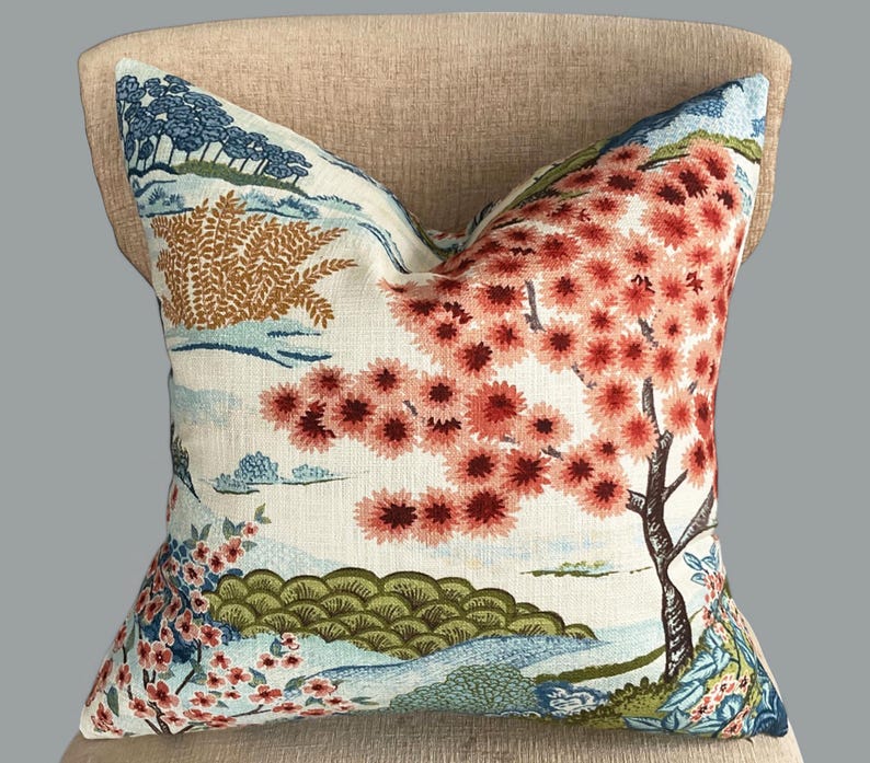 May include: A decorative throw pillow with a white background and a colorful floral pattern. The pattern features a large pink and red tree with smaller blue and green trees in the background. The pillow is perfect for adding a touch of nature to any room.