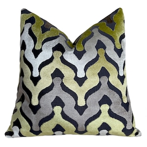 May include: A decorative throw pillow with a geometric pattern in shades of green, gray, and black. The pillow is made of a soft, velvety fabric.
