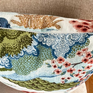 May include: A white pillow with a blue, green, and pink floral pattern. The pattern features stylized flowers, leaves, and clouds. The pillow is made of a soft, textured fabric.