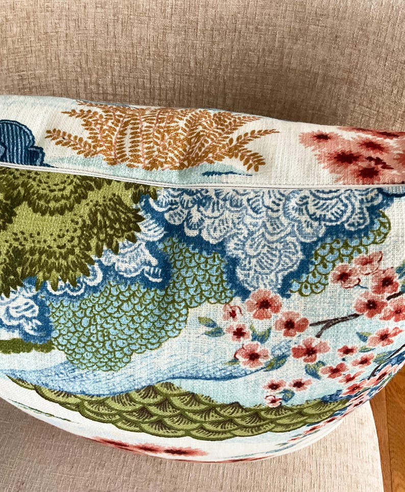 May include: A white pillow with a blue, green, and pink floral pattern. The pattern features stylized flowers, leaves, and clouds. The pillow is made of a soft, textured fabric.