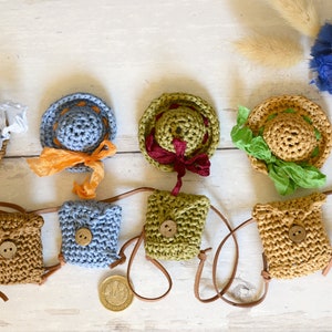 Op de afbeelding: Een verzameling miniatuur gehaakte hoeden en tassen. De hoeden zijn in verschillende kleuren, waaronder bruin, blauw en groen, en hebben verschillende versieringen, zoals linten en kant. De tassen zijn ook gehaakt en hebben leren banden.