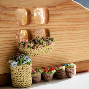 Könnte beinhalten: Ein Holzpuppenhaus mit einem Fensterkasten, der mit gehäkelten Blumen gefüllt ist. Unter dem Fenster befinden sich sechs kleinere gehäkelte Blumentöpfe in einer Reihe.