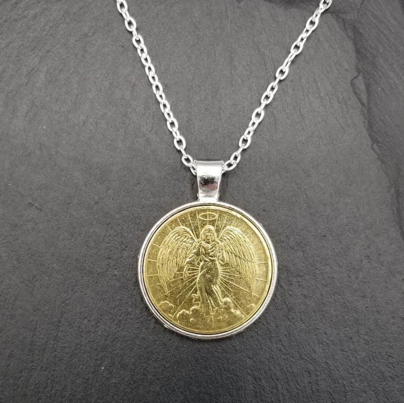 May include: A gold pendant necklace with a silver chain. The pendant features a detailed image of an angel with wings.