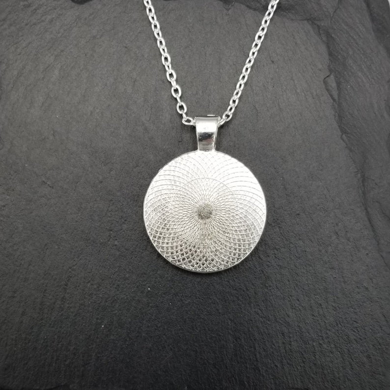 May include: Silver pendant necklace with a round, silver, patterned charm. The charm has a circular design with a raised center.