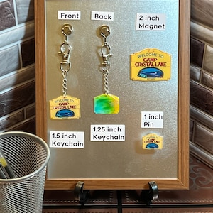 Puede incluir: Una exhibici&oacute;n de productos con tem&aacute;tica de Camp Crystal Lake. Incluye un im&aacute;n de 5 cm, un pin de 2,5 cm y un llavero de 3,8 cm. La parte trasera del llavero mide 3,2 cm. Todos los art&iacute;culos presentan el texto "WELCOME TO CAMP CRYSTAL LAKE EST 1995".