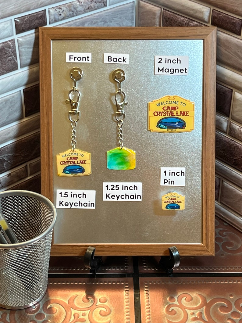 Puede incluir: Una exhibici&oacute;n de productos con tem&aacute;tica de Camp Crystal Lake. Incluye un im&aacute;n de 5 cm, un pin de 2,5 cm y un llavero de 3,8 cm. La parte trasera del llavero mide 3,2 cm. Todos los art&iacute;culos presentan el texto "WELCOME TO CAMP CRYSTAL LAKE EST 1995".