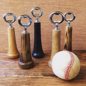 May include: A selection of bottle openers with wooden and black handles, and a baseball. The openers have a silver metal top. The wooden handles vary in colour and grain. The baseball is white with red stitching.