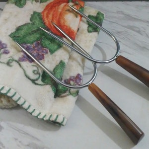 May include: Two silver metal skewers with brown wooden handles. The skewers are lying on a white fabric with a floral pattern.