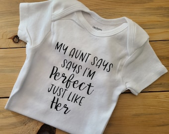 May include: White baby onesie with black text that reads "My Aunt Says I'm Perfect Just Like Her".