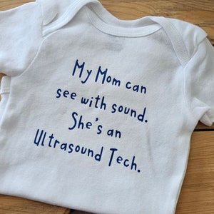 May include: White baby onesie with blue text that reads "My Mom can see with sound. She's an Ultrasound Tech."