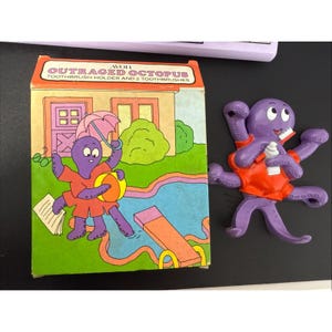May include: A vintage Avon "Outraged Octopus" toothbrush holder and two toothbrushes set. The box features a cartoon octopus with an umbrella and ball near a pool. The purple octopus figure is wearing an orange shirt.