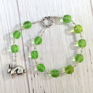 May include: A green glass bead necklace with a silver charm of a rabbit. The necklace has a silver clasp and is strung on a silver chain.