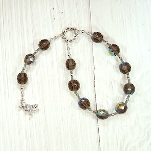 May include: A brown crystal beaded bracelet with a silver bird charm. The bracelet has a silver clasp and is made of faceted crystals.