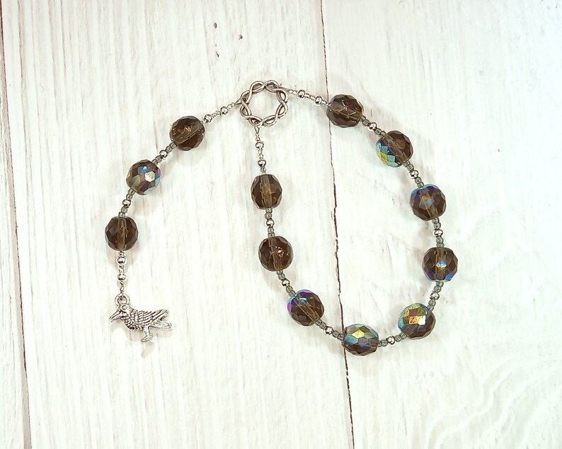May include: A brown crystal beaded bracelet with a silver bird charm. The bracelet has a silver clasp and is made of faceted crystals.