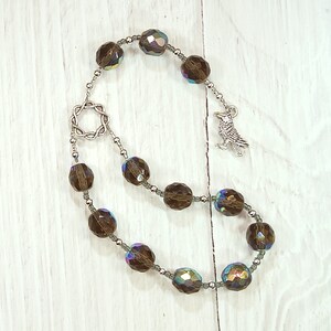 May include: A brown crystal beaded mala with a silver bird charm and a silver star-shaped pendant. The beads are iridescent and have a subtle sparkle.