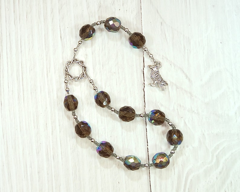 May include: A brown crystal beaded mala with a silver bird charm and a silver star-shaped pendant. The beads are iridescent and have a subtle sparkle.