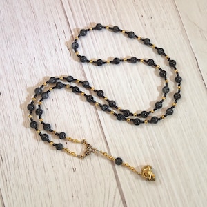 Peut inclure: Un collier de perles noires et dorées avec un pendentif en forme de crâne doré. Le collier est composé de petites perles rondes avec un motif noir et doré. Le pendentif en forme de crâne est un design simple sans détails.