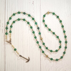 May include: A green and gold beaded necklace with an anchor pendant.