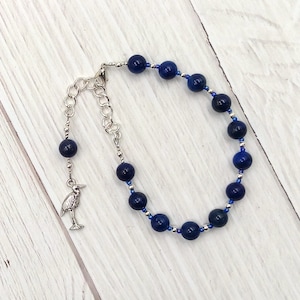 May include: A blue gemstone bracelet with a silver chain and a silver heron charm.