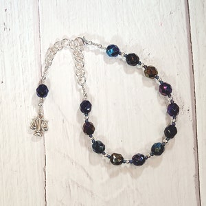 Puede incluir: Un brazalete plateado con un dije de balanza de la justicia y cuentas iridiscentes azules y moradas.