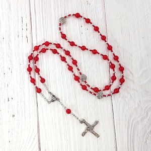 May include: Red beaded rosary necklace with a silver Celtic cross charm. The beads are small and round, and the cross is detailed with intricate designs.