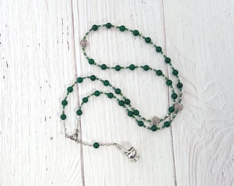 May include: A green and silver beaded necklace with a Celtic knot pendant. The necklace is made of small green beads and silver beads with Celtic knot charms.