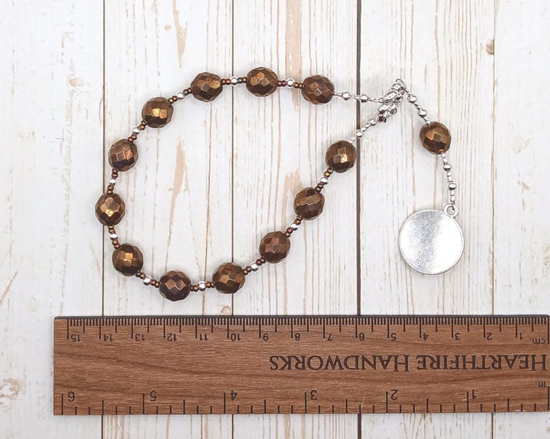 May include: A brown beaded necklace with a silver charm. The necklace is made of faceted beads and has a silver clasp. The charm is a round disc with a smooth surface.