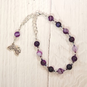 May include: Purple and white agate bead bracelet with a silver chain and a rainbow charm.