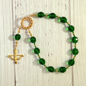 May include: A green and gold beaded rosary with a gold arrow charm.