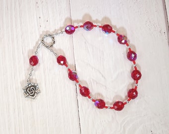 May include: A red crystal beaded mala with a silver rose charm. The beads are faceted and have a slight iridescent shimmer.