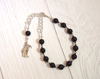 May include: A black beaded bracelet with a silver chain and a silver charm of a figure holding a scythe.