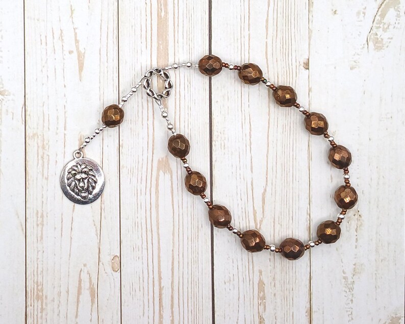 May include: A copper-toned beaded mala necklace with a silver lion head charm. The necklace is made of faceted beads and has a tassel at the end.