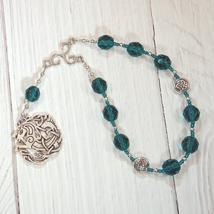May include: A teal green crystal beaded necklace with a silver Celtic knot pendant and a silver Celtic knot charm.