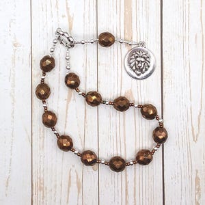 May include: A brown beaded necklace with a silver lion head charm. The beads are faceted and have a metallic sheen.