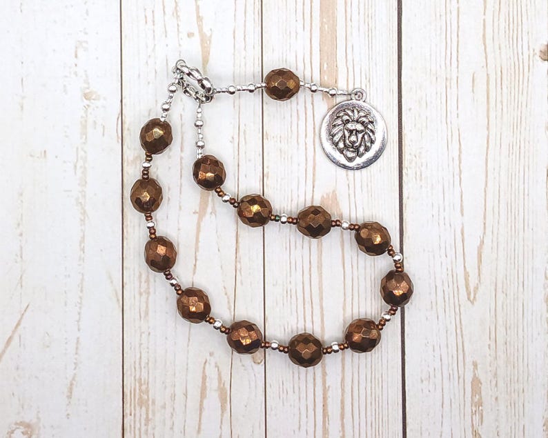 May include: A brown beaded necklace with a silver lion head charm. The beads are faceted and have a metallic sheen.