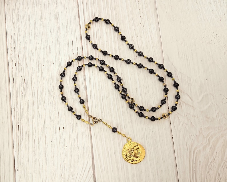 May include: A black and gold beaded necklace with a gold coin pendant featuring a profile of a person's face.