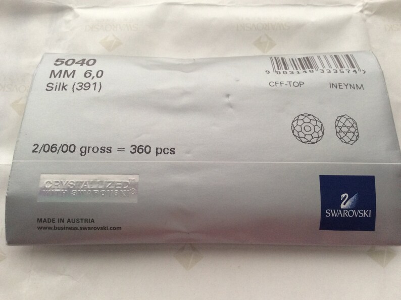 Pu&ograve; includere: Un pacchetto bianco con il testo "5040 MM 6,0 Silk (391)" e "2/06/00 gross = 360 pcs". Il pacchetto ha anche un logo Swarovski e il testo "CRYSTALIZED WITH SWAROVSKI".