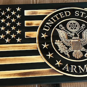 May include: A wooden American flag with a distressed black and brown finish. The flag features a gold seal with the words "United States Army" and an eagle design.