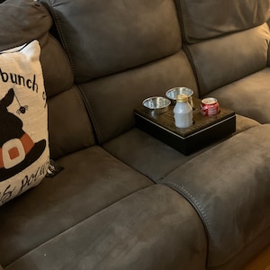 Op de afbeelding: Een bruine bank met een kussen waarop "bunch of" staat en een houten dienblad met twee metalen bekers en een blikje frisdrank.