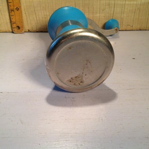 May include: A blue and silver hand-crank food grinder. The grinder has a round base and a crank handle.